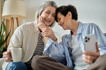 Téléchargez les photos : Deux femmes âgées assises sur un canapé et absorbées dans leur téléphone. - en image libre de droit