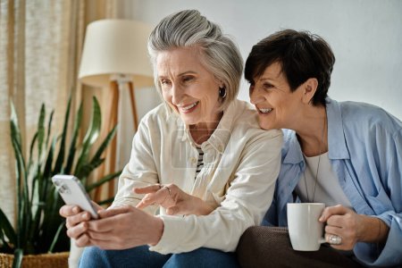 Dos mujeres mayores sentadas en un sofá, absortas en un teléfono celular.