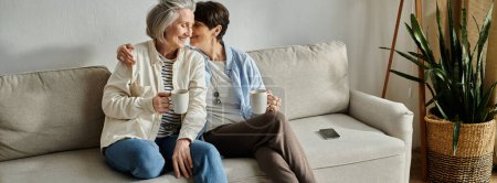Dos personas mayores, una pareja lesbiana madura amorosa, se sientan de cerca en un sofá.