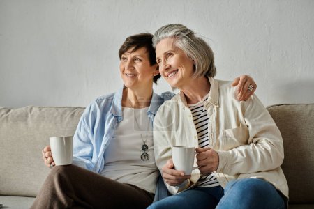Lesbianas mayores disfrutando de una acogedora pausa para tomar café en un sofá.