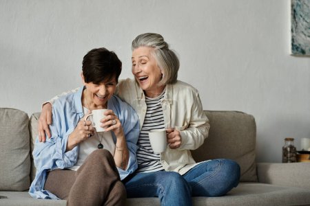 Two older women gracefully enjoy coffee on a cozy couch.