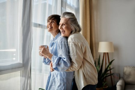 Photo for Two elder women hugging warmly in front of a bright window. - Royalty Free Image