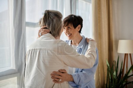 Photo for Two elderly women share a heartwarming hug in front of a luminous window. - Royalty Free Image