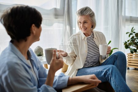 Two senior women enjoying a conversation on a sofa with coffee.
