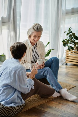 Photo for Two women, a loving mature lesbian couple, sitting on the floor chatting and connecting. - Royalty Free Image