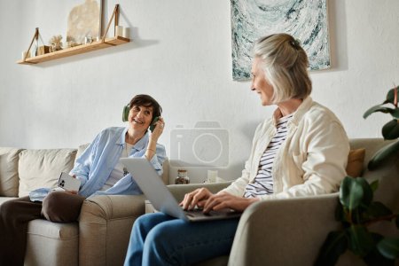 Téléchargez les photos : Two women engage in conversation while using a laptop on a cozy couch. - en image libre de droit
