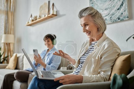 Foto de Dos mujeres se sientan en un sofá, enfocadas en la pantalla de su portátil. - Imagen libre de derechos