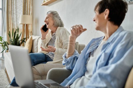 Two women chatting on phone while relaxing on couch.