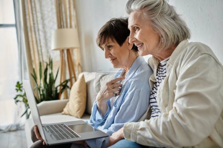 Two older women enjoy using a laptop while sitting on a couch together.