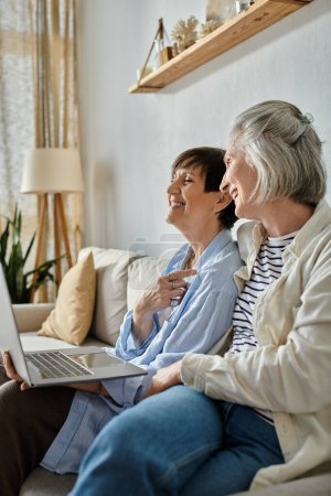 Two elderly women sit on a couch, engrossed in using a laptop.