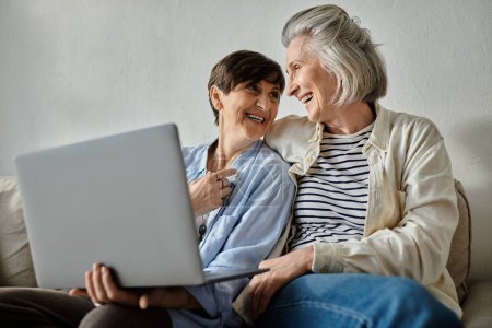 Zwei ältere Frauen sitzen auf einer Couch, mit einem Laptop beschäftigt.