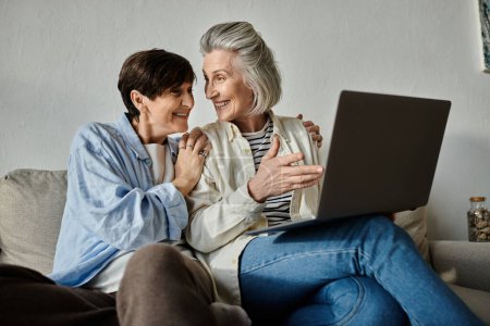 Two older women sharing a laptop on a cozy couch.