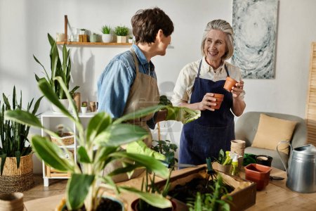Téléchargez les photos : Deux femmes dans des tabliers profitant d'une conversation sur les plantes dans un cadre confortable à la maison. - en image libre de droit