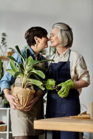 Zwei Frauen in Schürzen küssen sich vor Topfpflanze.