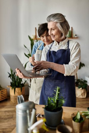 Zwei ältere Frauen in gemütlicher Küche in Laptop vertieft.