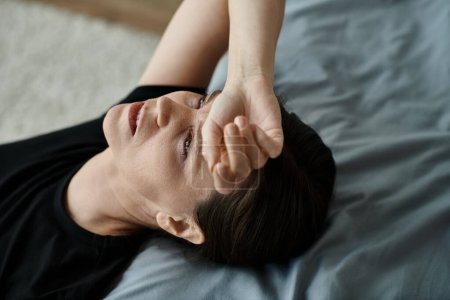 Middle-aged woman laying on bed with hand on head in a moment of introspection.