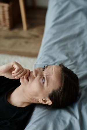 A woman with hand on face, lying on bed in thought.