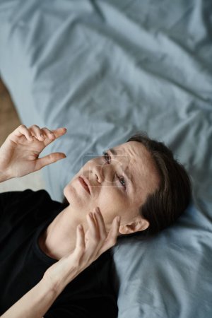 Middle-aged woman embraces her face, displaying distress on a bed.