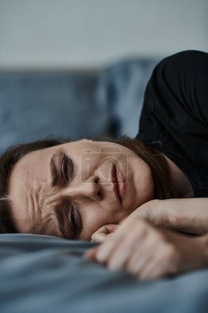 A woman lays on bed, hand on face.