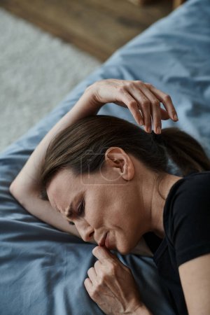 Middle-aged woman lying in bed, hand on head, lost in thought.