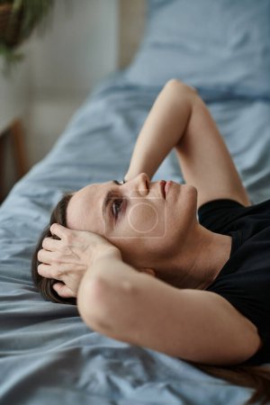 Foto de Woman laying on bed with hands on head, reflecting on inner turmoil. - Imagen libre de derechos