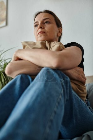 Photo for Middle-aged woman sits on couch with arms crossed. - Royalty Free Image