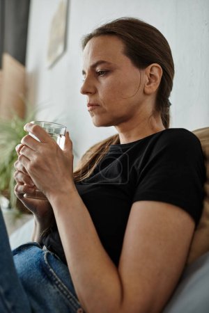 Woman in contemplation on couch holding water.