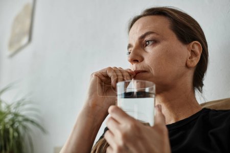 A woman finds solace on her couch, holding a glass of water.