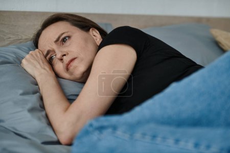 Middle-aged woman lying in bed, head propped on hand, lost in deep thought.