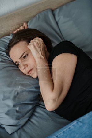 Middle-aged woman laying down, holding head in hand with contemplative expression.