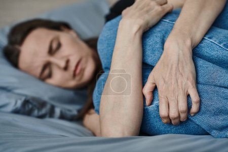 Photo for Middle-aged woman laying peacefully in bed with hands resting on her stomach. - Royalty Free Image