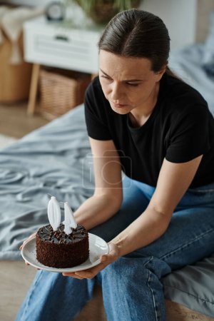 Woman holding a cake while sitting on her bed.