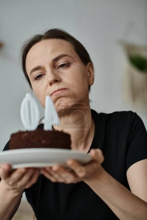 Photo for Middle-aged woman holding a cake with the number 40 on it, celebrating a birthday. - Royalty Free Image