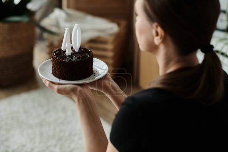 Téléchargez les photos : A middle-aged woman holding a birthday cake on a plate in a home setting. - en image libre de droit