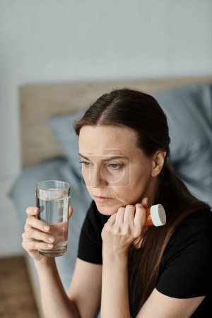 A woman peacefully holding a glass of water on her bed.