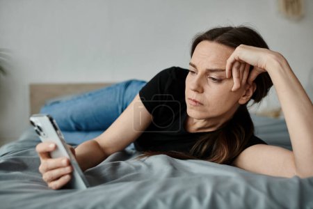 Middle-aged woman laying on bed, absorbed in her phone screen.