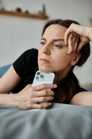 A middle-aged woman lies on a bed holding a phone.