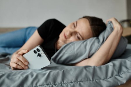 Middle-aged woman laying in bed, holding phone, lost in thought.