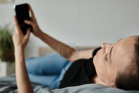 Téléchargez les photos : A woman in bed holds her phone, lost in online therapy during a mental breakdown. - en image libre de droit
