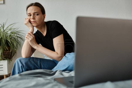 Woman sits on bed, absorbed in laptop screen.