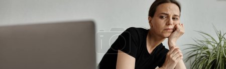 A middle-aged woman sits in front of her laptop, connecting to an online therapy session.