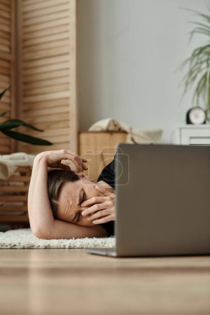 Middle-aged woman lying on floor with laptop, seeking online therapy.