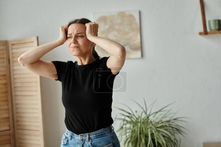 Foto de Woman in distress holds head in living room. - Imagen libre de derechos