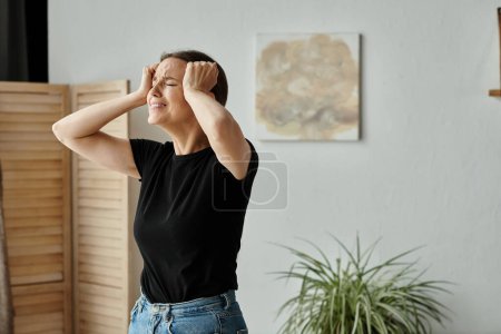 Middle-aged woman expresses distress with hands on head in cozy living room.