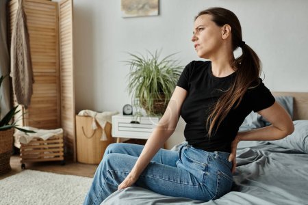 Woman sitting on bed, clutching her lower back in pain, struggling with depression.