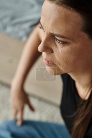 A middle-aged woman sits and cries, struggling with depression.