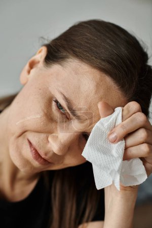 Middle aged woman wiping her face with a tissue during a moment of emotional release.