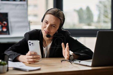 Photo for Middle-aged woman in headset having a phone conversation while seated at office desk. - Royalty Free Image