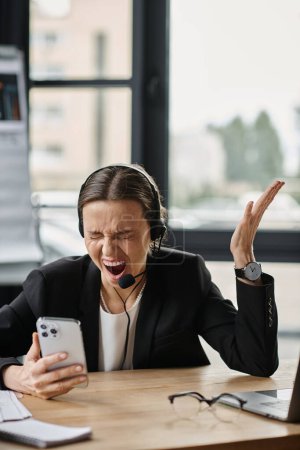 Middle-aged woman in distress shouting at smartphone while seated at desk.