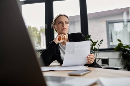 Middle aged woman sitting at desk, reading paper with a concerned expression.